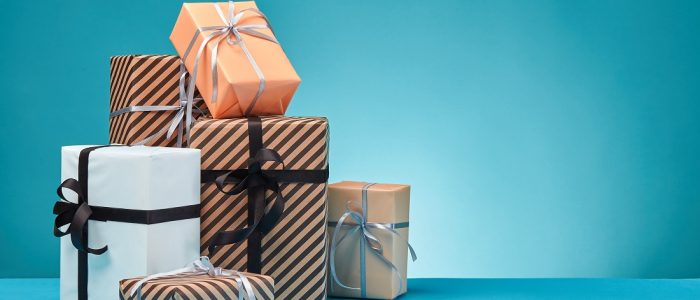 Different sizes, colorful, striped and plain paper gift boxes tied with ribbons and bows on a blue surface and background. Close-up, copy space.